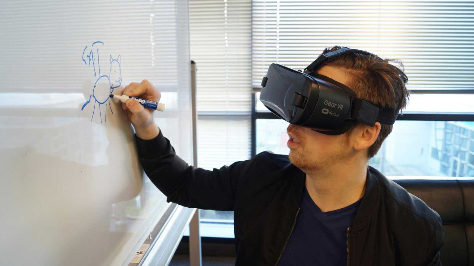 A man wearing a VR headset drawing a cat on a whiteboard in an office environment.